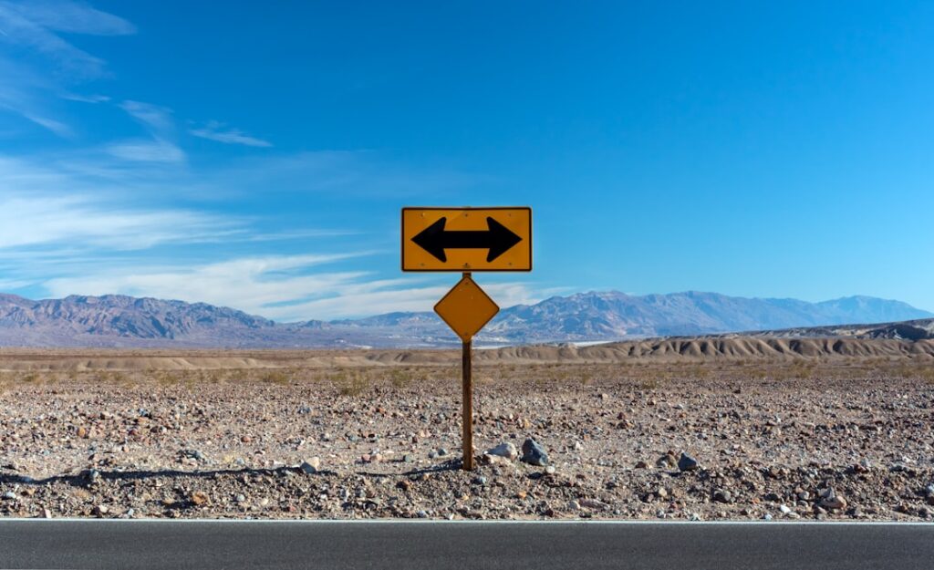Stock photograph of a road sign in open desert country with arrows pointing in two opposite directions.