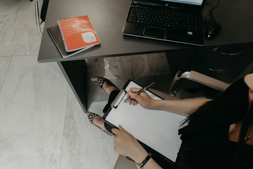 Stock photograph of a person writing on a clipboard beside a laptop at a desk, used to illustrate an article about content quality review