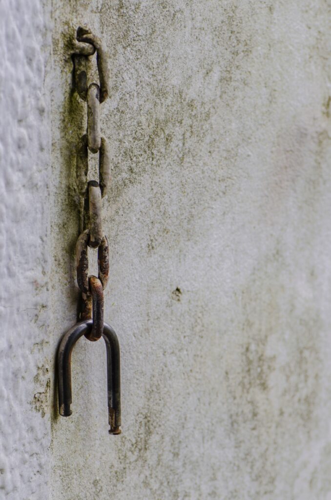 An old rusty chain hanging against a weathered, textured wall. Stock photograph used as an illustration of links.