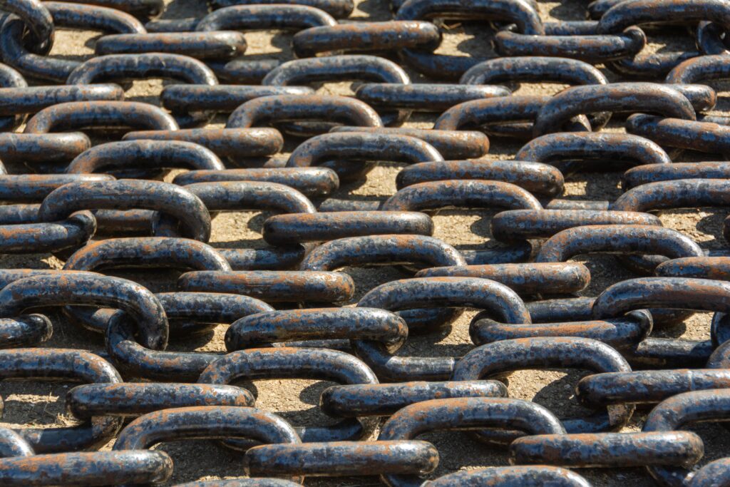 Stock photograph of rusty metal chains lying outdoors in sunlight, used as a metaphor for chained links; not a diagram of any real link scheme