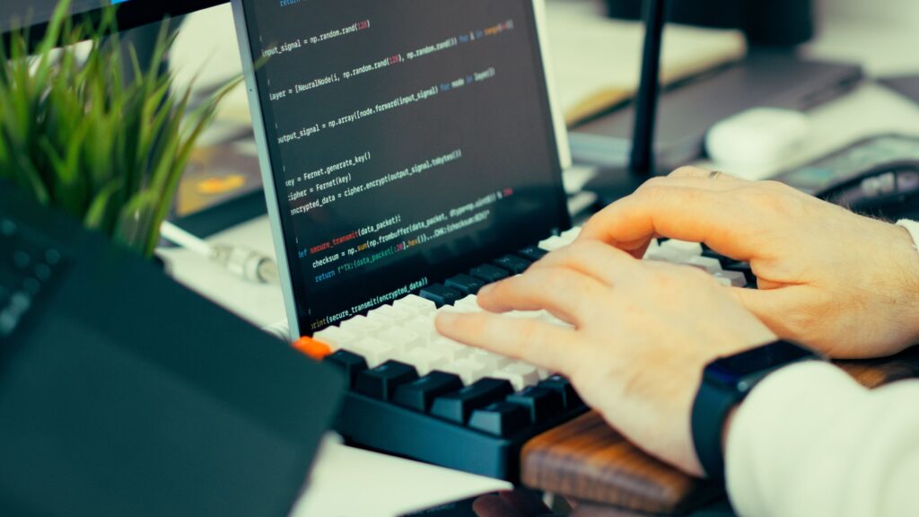 A developer typing at a keyboard with lines of code visible on the screen behind their hands.