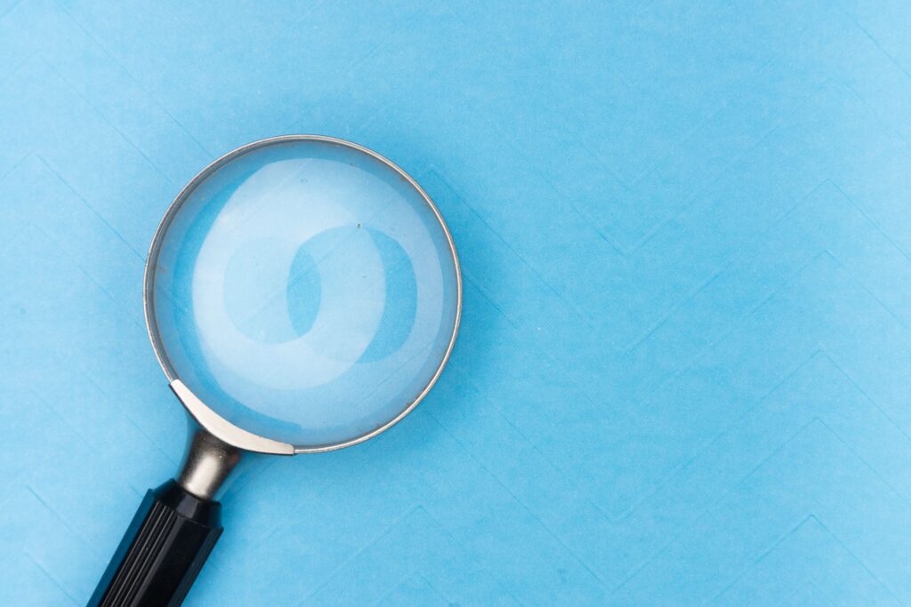 Stock photo of a magnifying glass lying on a plain blue surface, used to illustrate research
