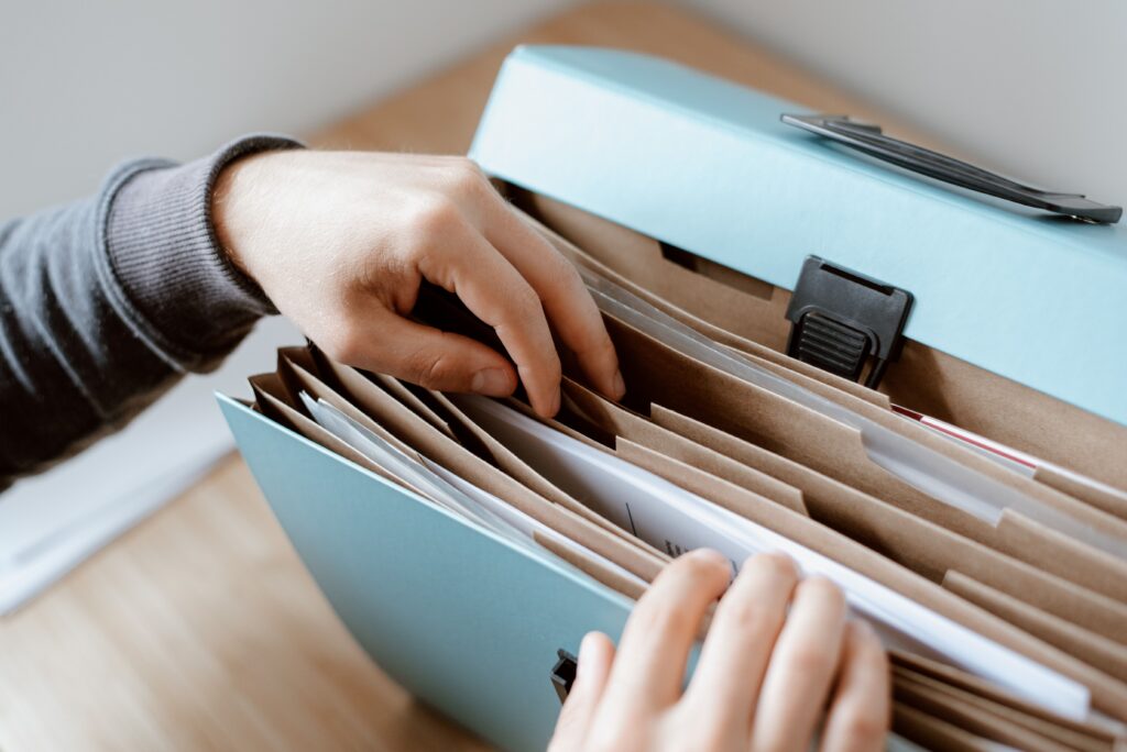 Stock photograph of hands sorting papers in a blue folder on a wooden table, illustrating duplicate pages