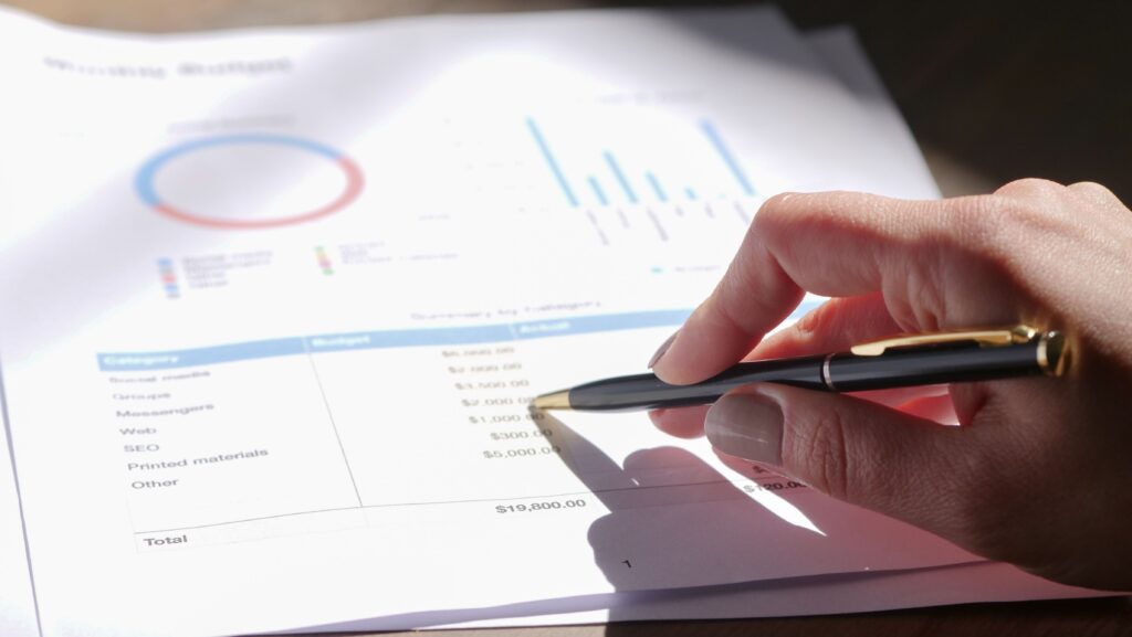 Stock photograph of a hand holding a pen over printed charts and columns of figures on a desk. It is a generic stock image and not a screenshot of a real content audit or any client data.